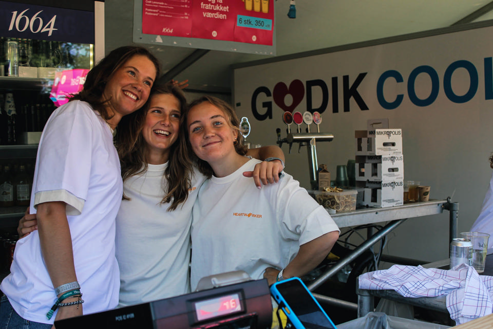 Tre frivillige bartendere på en festival står foran en Godik kølevogn