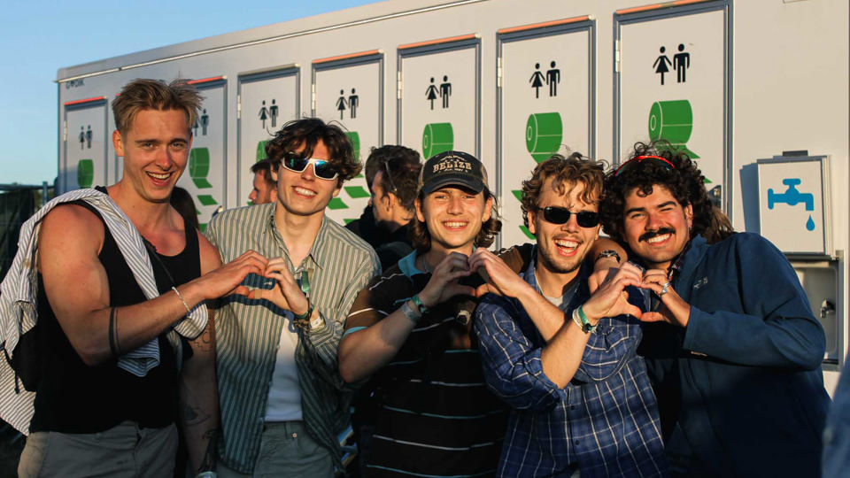 Unge festivalgæster foran Godiks toiletvogne ved et udendørs event