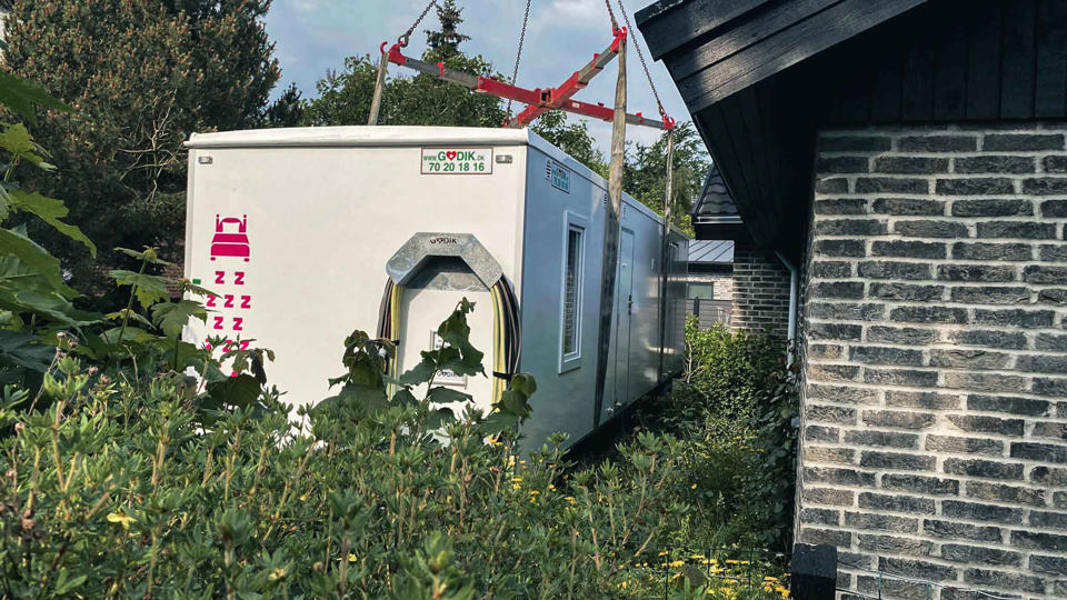 En beboelsesvogn bliver flyttet over hækken og placeret i haven til et parcelhus