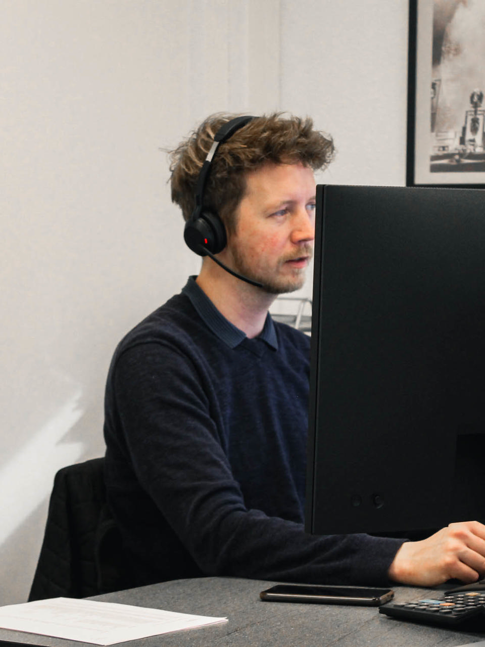 En Godik udlejningskonsulent taler i telefon med en kunde foran computeren